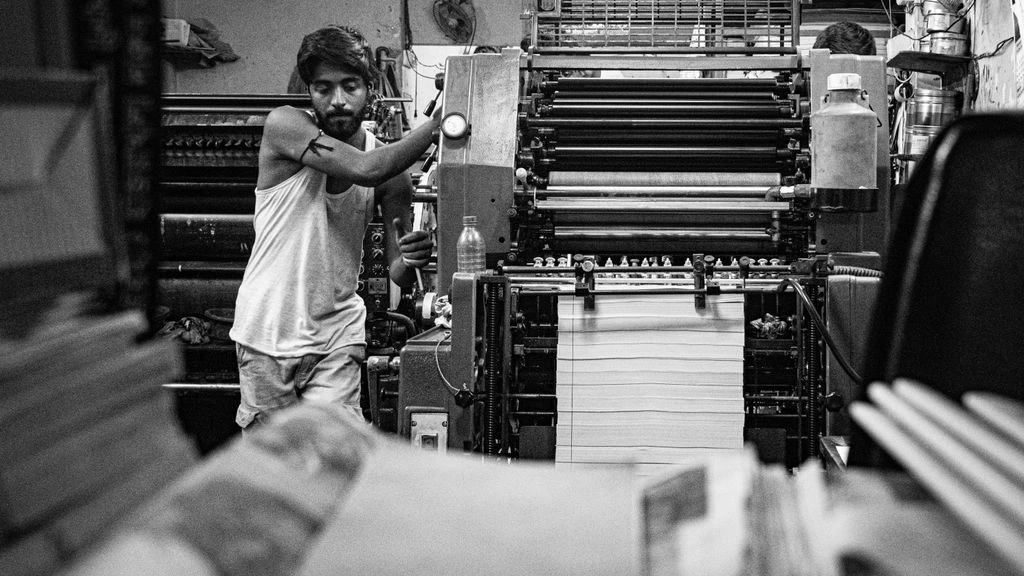 A working print-shop bench in the 1Stop Poster Shop Phoenix production facility, with a freshly printed stack of posters and a color-bar proof sheet in the foreground.